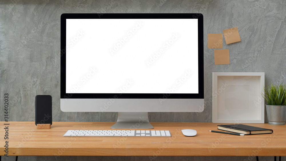 Close up view of blank screen desktop computer with sticky note, frame and office supplies with loft grey wall Close up view of blank screen desktop computer with sticky note, frame and office supplies with loft grey wall