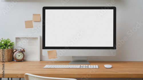Close up view of mock up desktop computer with sticky note and decoration on wooden desk with white wall