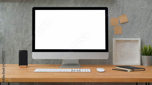 Close up view of blank screen desktop computer with sticky note, frame and office supplies with loft grey wall