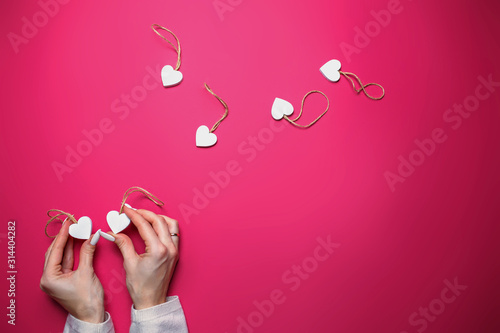 Small white wooden hearts on pink background with copy space. Saint Valentine's day card with woman holding hearts in hands on pink background.