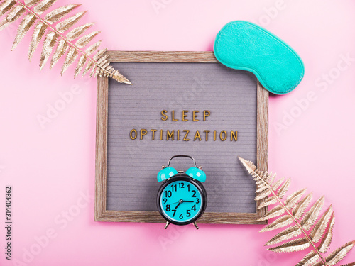 Sleep optimization text composed on wooden letter board with green sleeping mask, alarm clock, golden branches. Better healthy sleep tips concept photo