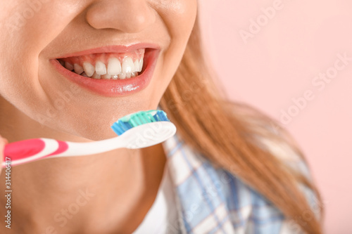 Young woman brushing teeth on color background, closeup