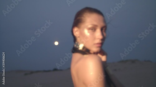 Portrait of young woman at night in the desert dancing in front of the full moon.