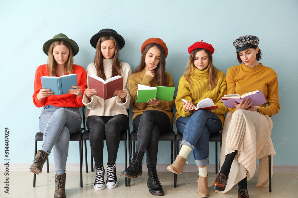 Obraz premium Young women with books sitting near color wall