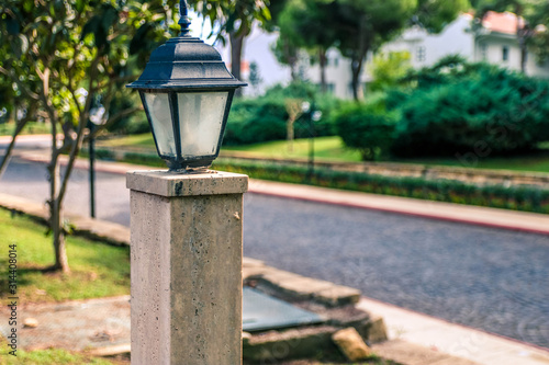 A street garden ground lantern mounted on a green lawn in a park near a stone path way for walks in a summer garden.
