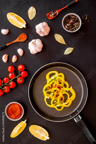 Cooking food concept. Pasta on frying pan near spices and vegetables on black background top-down