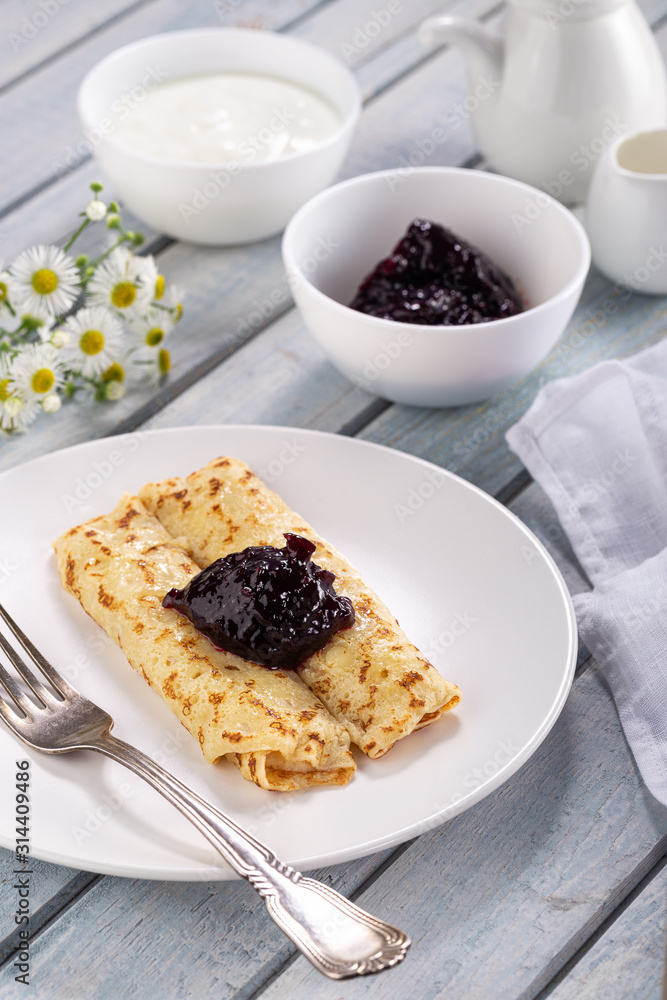 Homemade pancakes with cream cheese and berry jam on a plate, selective focus. Wooden table