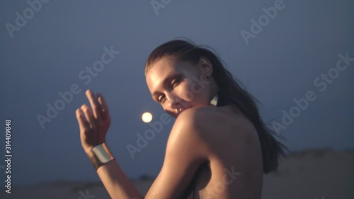 Portrait of young woman at night in the desert dancing in front of the full moon.