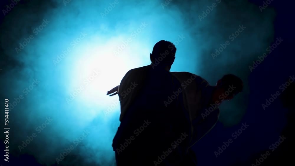 Two fighters Practicing aikido technique, silhouettes of masters in dark studio with smoke and lighting. Slow motion. Close up. Two fighters Practicing aikido technique, silhouettes of masters in dark studio with smoke and lighting. Slow motion. Close up.