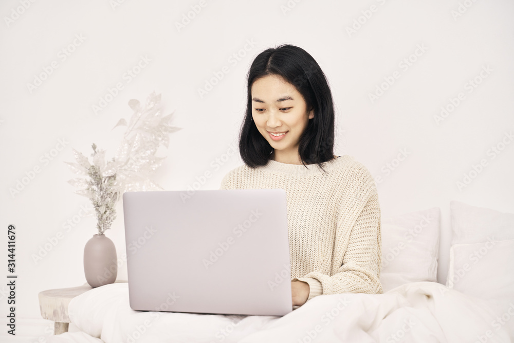 Beautiful woman freelancer Asian appearance with dark hair hairstyle Bob wears sweater has an attractive white smile works at laptop, writes post in blog about personal life career dreams of traveling Beautiful woman freelancer Asian appearance with dark hair hairstyle Bob wears sweater has an attractive white smile works at laptop, writes post in blog about personal life career dreams of traveling