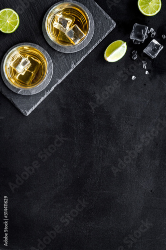 Bar background with whiskey and ice on black desk top-down frame copy space
