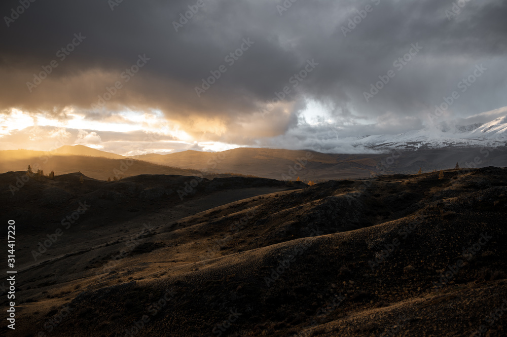 gloomy landscape of high gray mountains under dense gray clouds with glimmers of bright sunlight