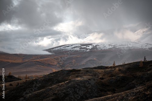 gloomy landscape at sunset day of a giant snowy mountain range with glaciers towering over the autumn valley