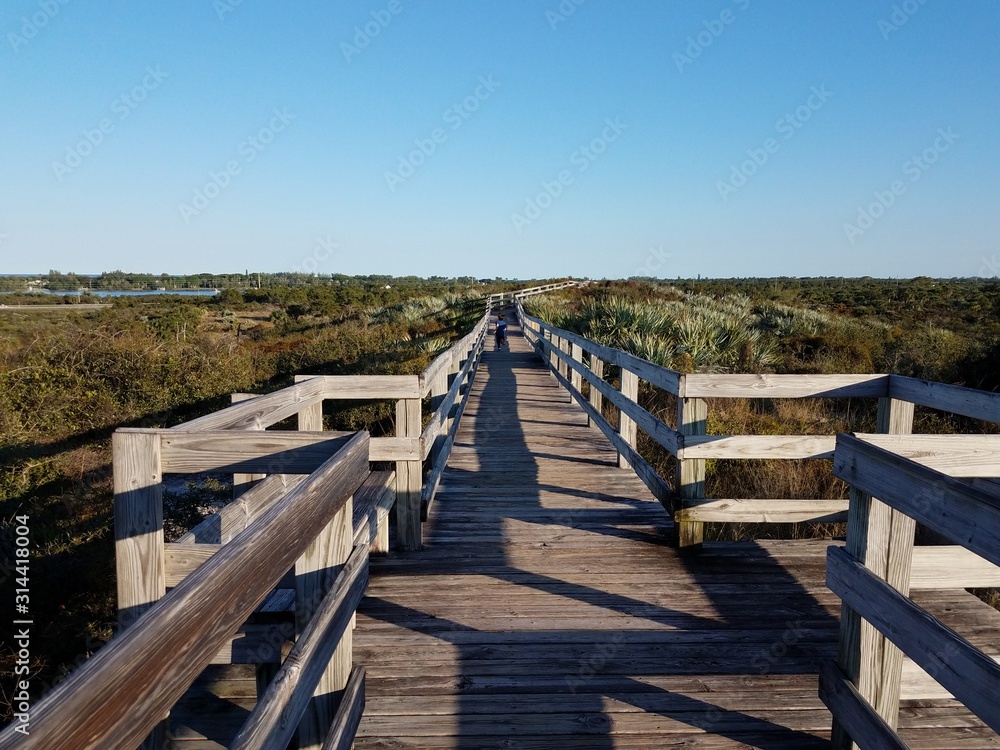child running on wood boardwalk or trail with plants and sky in Florida