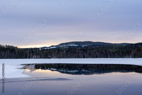 Open calm spot in a frozen lake with reflections of forest and a mountain. © Lars-Ove Jonsson