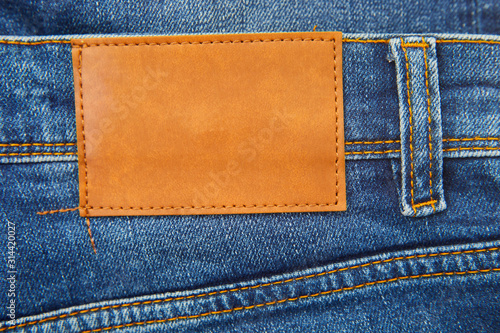 Brown leather empty copy space label texture. Back side of blue denim jeans trousers background.