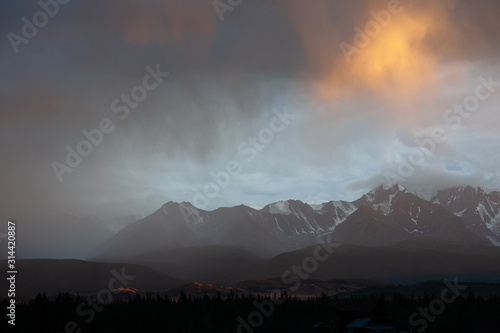 epic landscape of a giant snowy mountain range under a hurricane of rain and sun