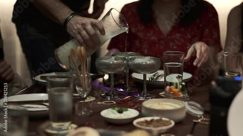 Pouring water in the silver glasses during friends dinner in restaurant. Concept of Greece, purity, healthcare, wellbeing, happy family, party with friends