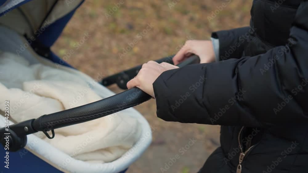 Close up of woman hands. Mom hands are rolling a stroller with a sleeping baby in an autumn or spring park. Close up of woman hands. Mom hands are rolling a stroller with a sleeping baby in an autumn or spring park.