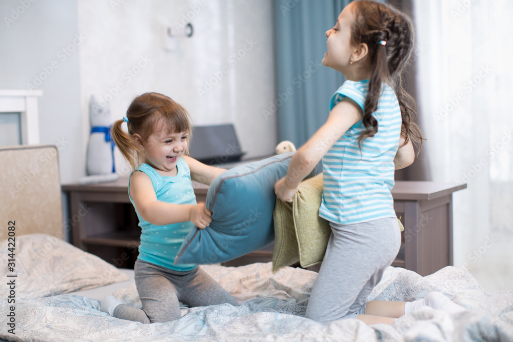 children sisters have fun playing with pillows in bedroom at home