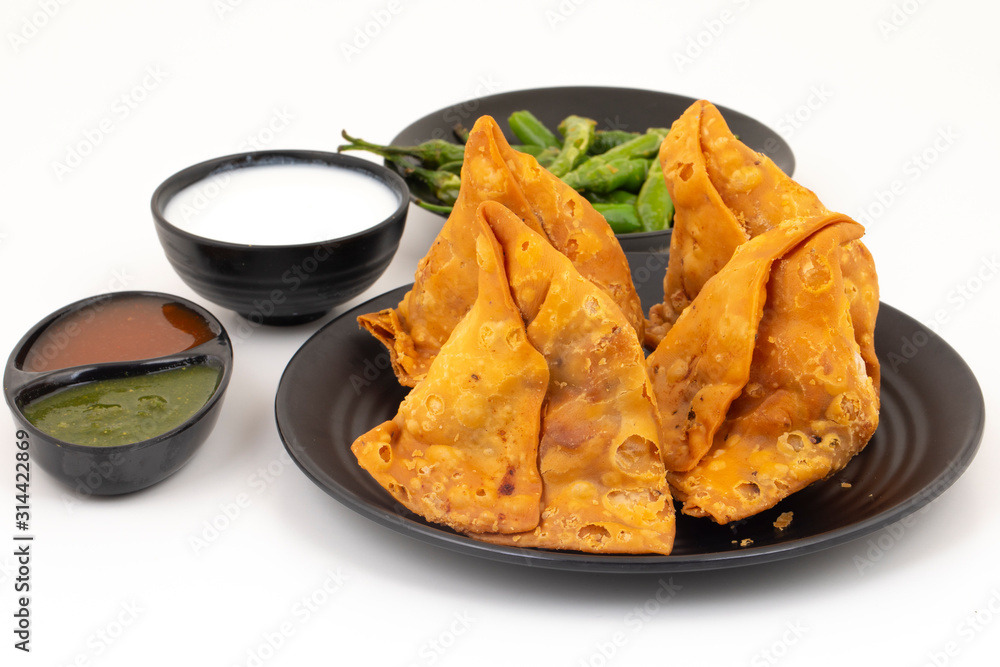 Indian Street Food Samosa or Samosas is a Crispy And Spicy Triangle Shape Snack Which Has Crisp Outer Layer of Maida & Filling of Mashed Potato, Peas And Spices. Served With Chutney, Ketchup or Curd