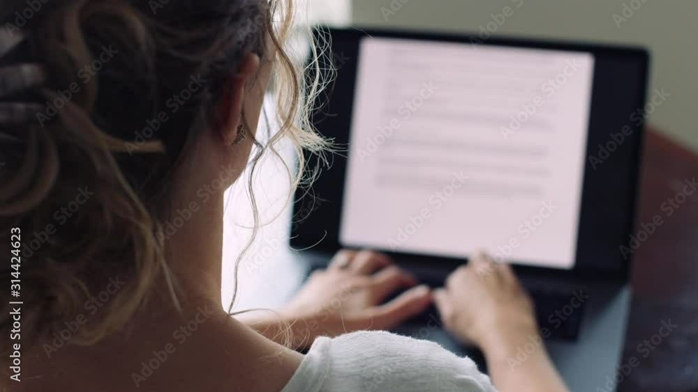 Woman with curly hair types quickly and thoughtfully on a laptop 8K
