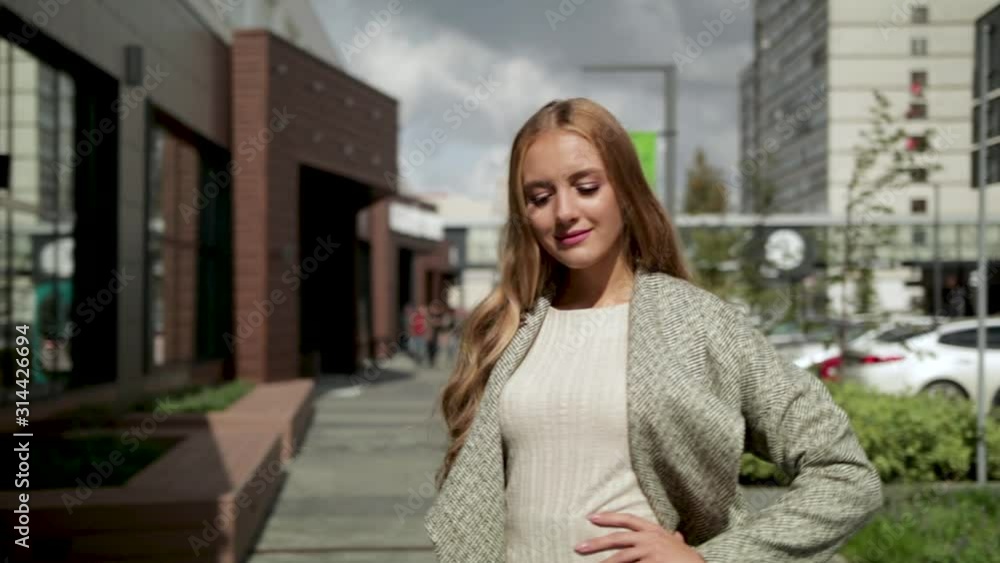 Young beautiful girl in a coat walking down the street, posing and smiling, city, summer Young beautiful girl in a coat walking down the street, posing and smiling, city, summer