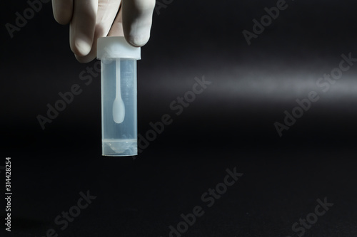 A female hand in a white medical glove holds the lid of a sterile white plastic container or jar for stool or feces analysis or coprology test on a black background. Horizontal close-up
