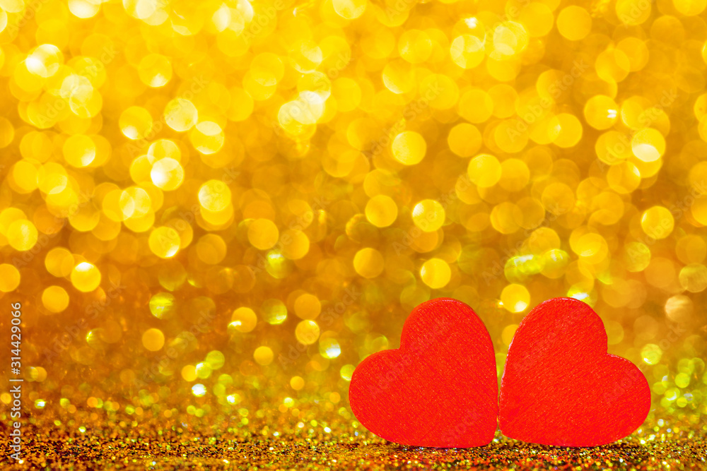Red little decorative hearts against gold yellow sparkle glitter background with amazing bokeh lights. Love or romantic Valentine day concept. Holiday background