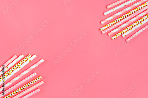 Drinking paper straws for party with golden, white, pink stripes on pink pastel background with copy space. Top view of colorful paper disposable eco - friendly straws for summer cocktails. Flat lay  
