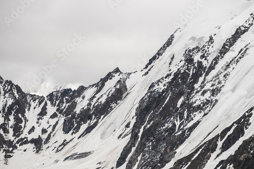 Atmospheric minimalist alpine landscape of big snowy mountain with massive glacier. Cloudy sky over great rocky mountains. Glacier tongue near snowbound mountainside. Majestic scenery on high altitude