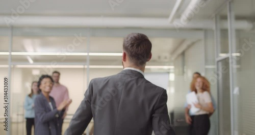 Backside view of overjoyed company chief walking through office room and throwing his jacket. Office staff congratulating male boss with signing great deal and giving him high five.