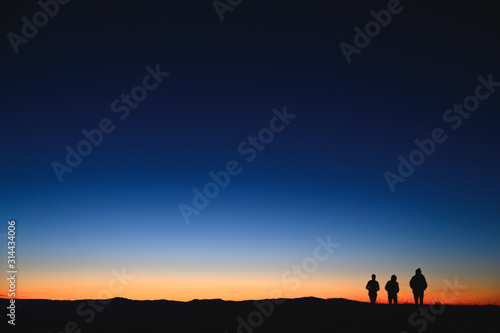 Three tourist walking in morning mountains. Sunrise colors in background