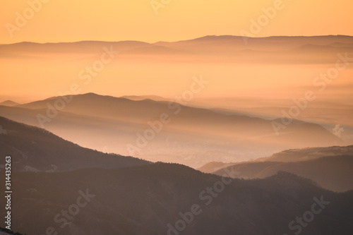 Orange colors of sunrise in mountains, morning mist in the valley, edit space