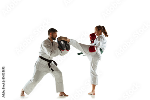 Junior in kimono practicing hand-to-hand combat with coach, martial arts. Young female mongol fighter with green belt training on white studio background. Concept of healthy lifestyle, sport, action.