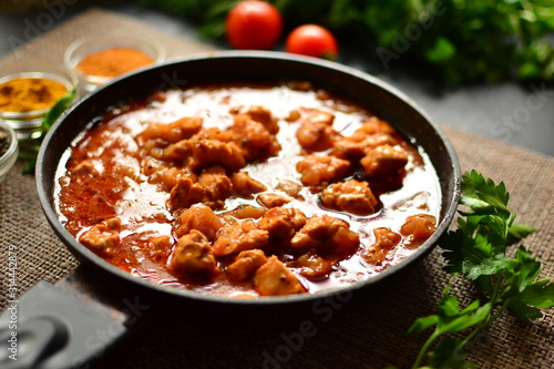 Indian food. Chicken Tikka Masala in a pan on a dark background. Appetizing meat with curry and tomato sauce, gravy with various spices. Delicious food, vertical view from the side.