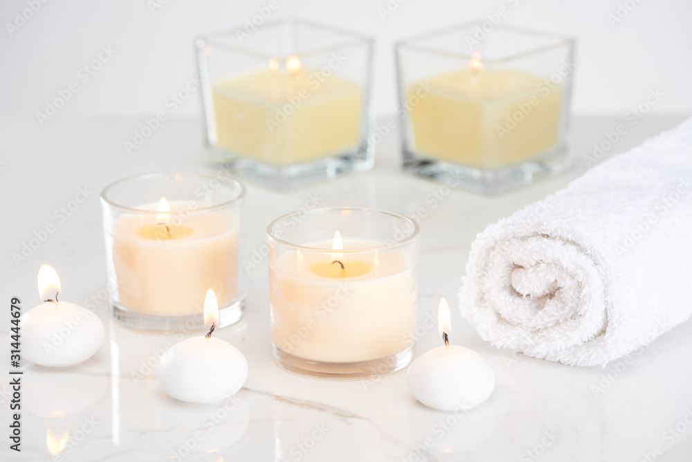 burning white candles in glass and rolled towel on marble white surface