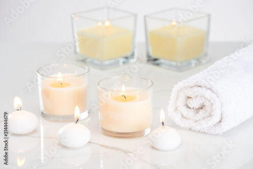 burning white candles in glass and rolled towel on marble white surface