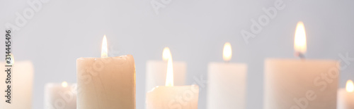selective focus of burning white candles glowing isolated on grey, panoramic shot photo