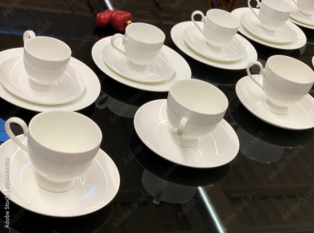 White cups with saucer standing on table. Cutlery in restaurant. Service on black table.