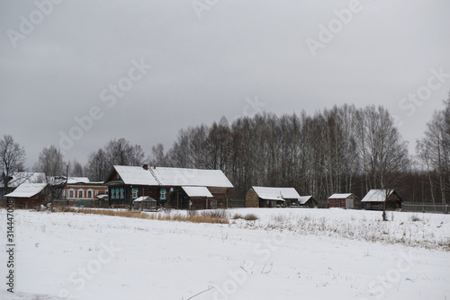 Traditional village house and fence in winter in cloudy weather. Old northern architecture of Russia. Log cabin is called izba