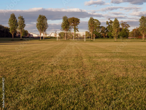Football soccer field with goalpost in the background, freshly cut grass surface, nobody, cloudy sky, Factory roof in the background.