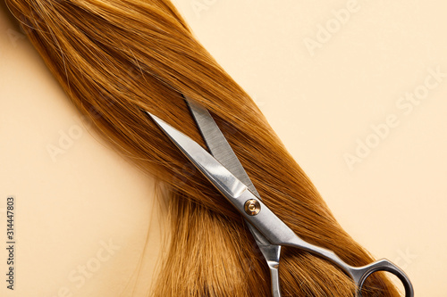 Top view of scissors on brown hair on beige background