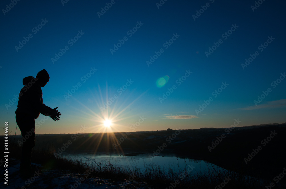  Silhouetted men on a background of blue sky and sunny sunset. Man with hands up