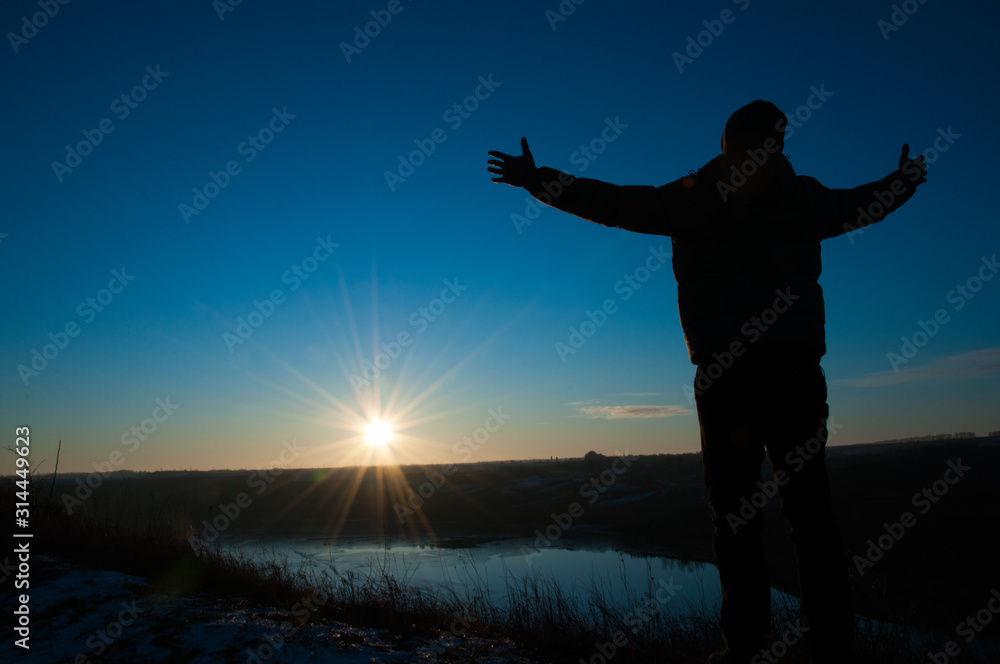 Fototapeta premium Silhouetted men on a background of blue sky and sunny sunset. Man with hands up