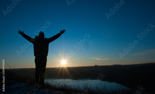Pray. Silhouetted men on a background of blue sky and sunny sunset. Man with hands up