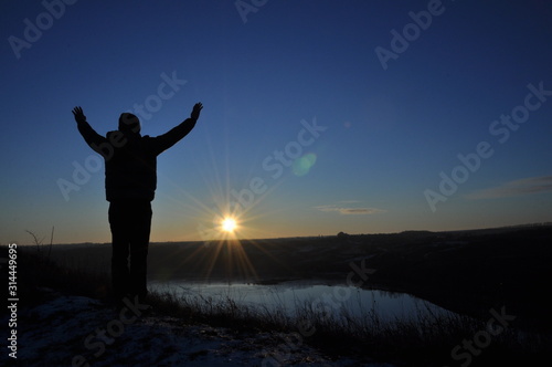 Silhouetted men on a background of blue sky and sunny sunset. Man with hands up