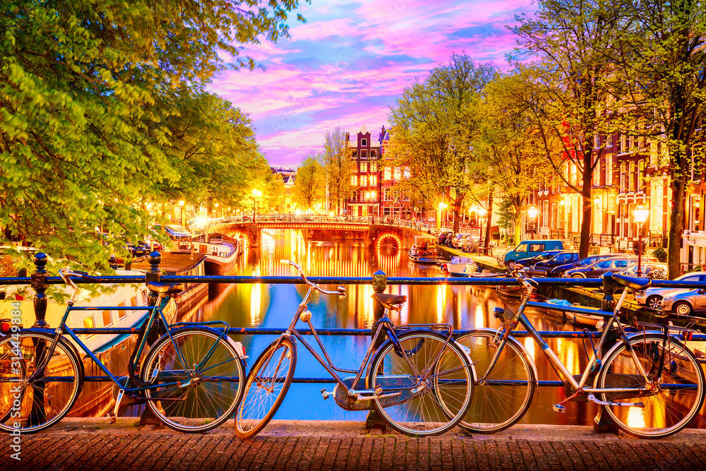 Old bicycles on the bridge in Amsterdam, Netherlands against a canal during summer twilight sunset. Amsterdam postcard iconic view.