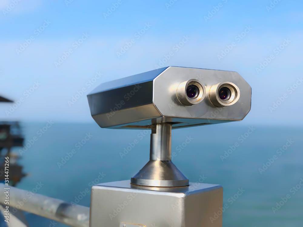 Paid outdoor tourist telescope made of stainless steel on the sea coast over blue sky background