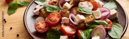 close up view of delicious Italian vegetable salad panzanella served on plate on wooden table, panoramic shot